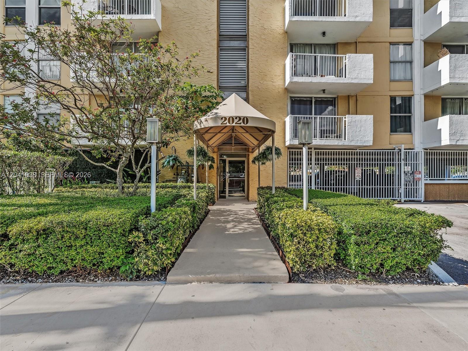 A beige apartment building entrance features a tan awning over a glass door and walkway — 2020 NE 135th St # 601, North Miami FL 33181, NORTH MIAMI, FL