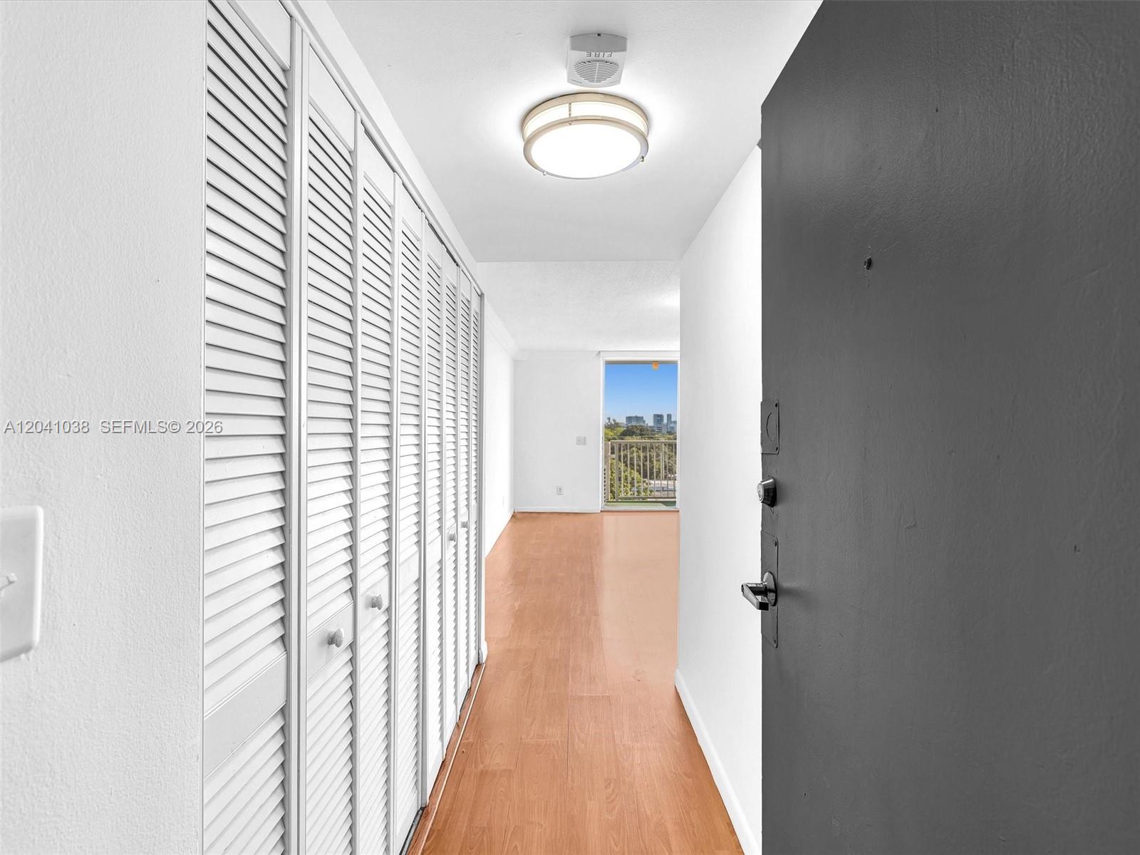 A hallway with white louvered closet doors leads to a room with a balcony view — 2020 NE 135th St # 601, North Miami FL 33181, NORTH MIAMI, FL