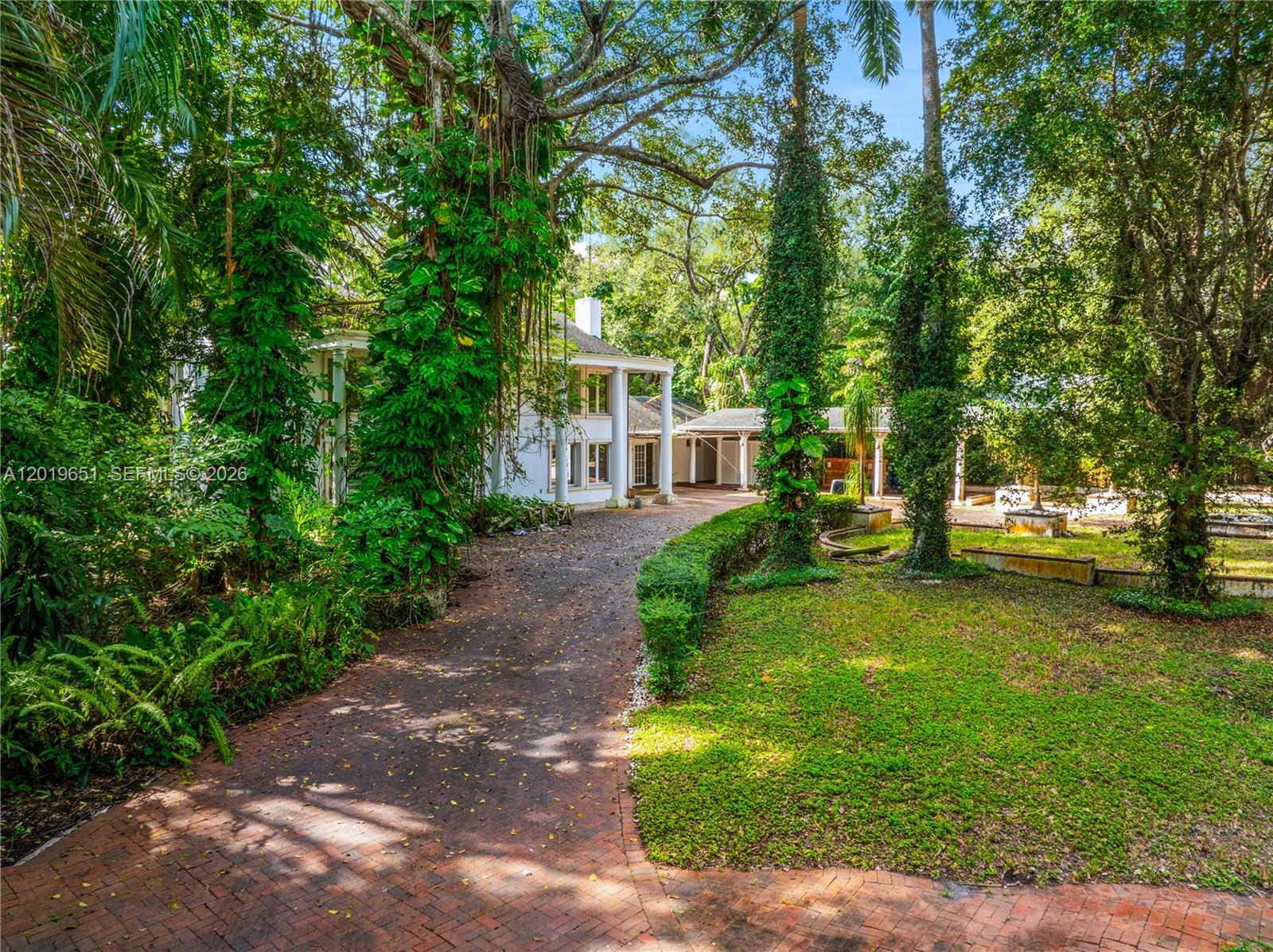 A brick driveway leads to a white two-story house with columns surrounded by lush trees — 3720 Poinciana Ave, Miami FL 33133, MIAMI, FL