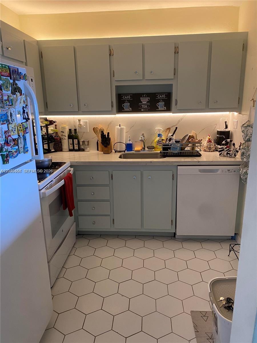 A kitchen features light gray cabinets, white countertops, a white appliance suite, and hexagonal floor tiles — 1465 NE 123rd St # 409, North Miami FL 33161, NORTH MIAMI, FL