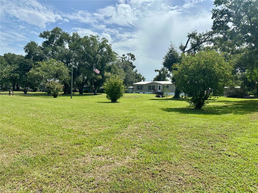 A grassy yard with scattered trees and an American flag leads to a mobile home — 8528 AVON LADY PLACE, PLANT CITY, FL