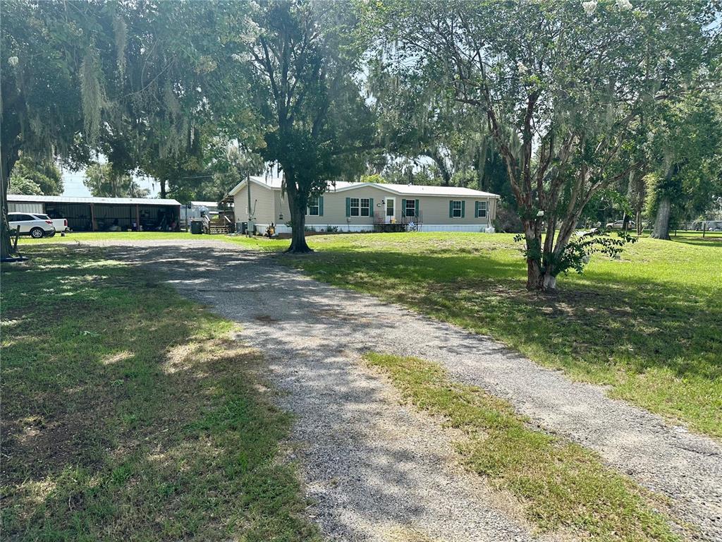 A gravel driveway leads to a single-story manufactured home with a detached metal carport — 8528 AVON LADY PLACE, PLANT CITY, FL