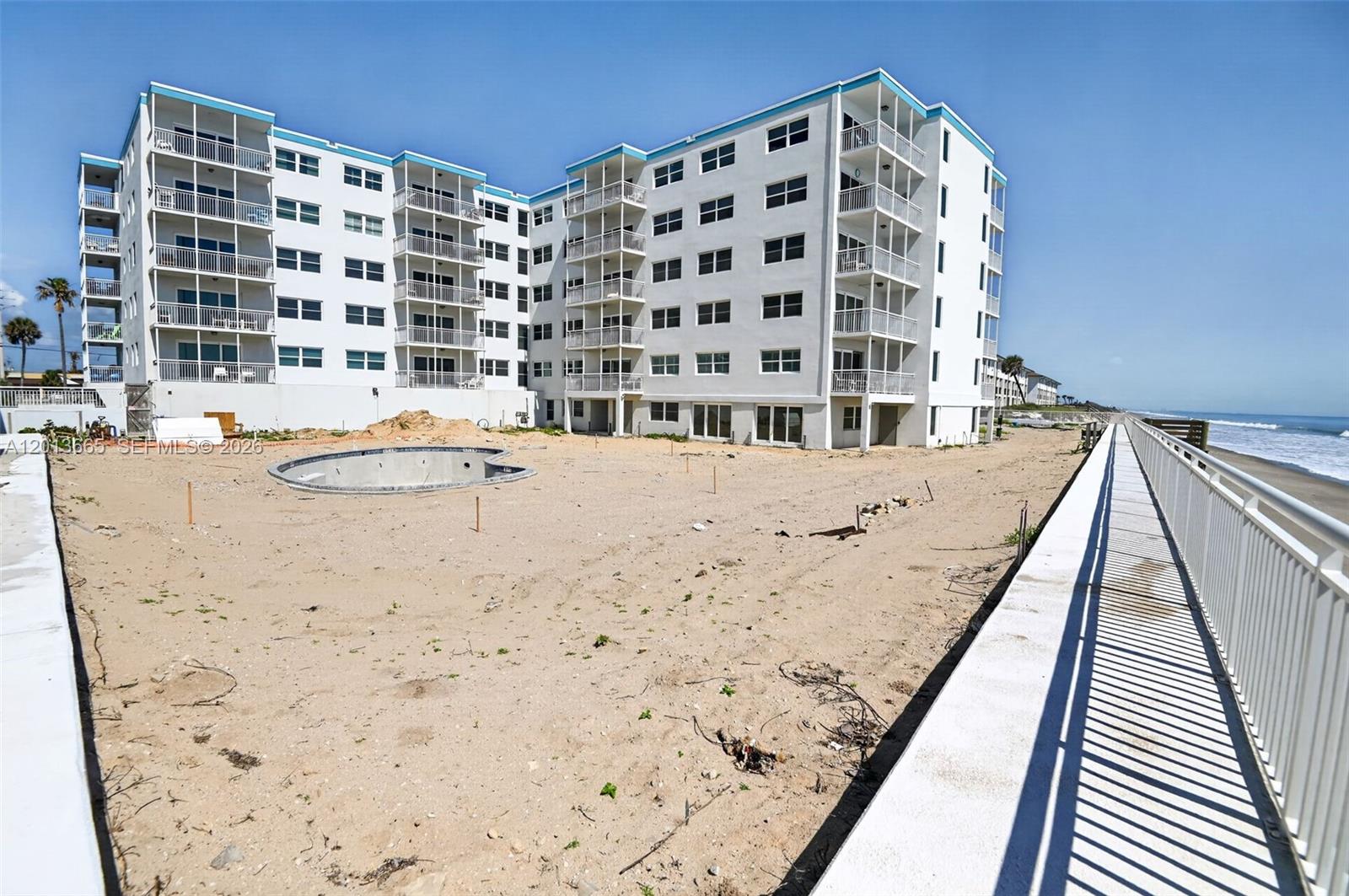 A multi-story white apartment building stands beside a sandy lot with an unfinished pool — 205 Highway A1A Unit 502, Satellite Beach FL 32937, SATELLITE BEACH, FL