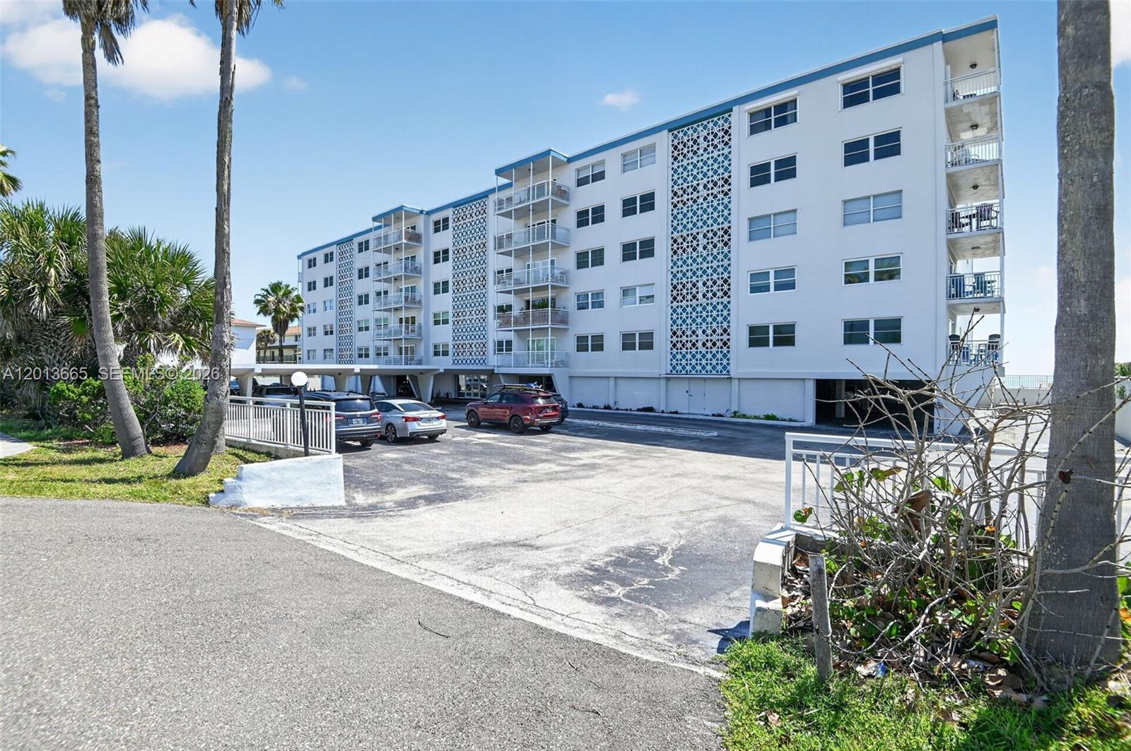 A multi-story apartment building with a parking lot and palm trees in the foreground — 205 Highway A1A Unit 502, Satellite Beach FL 32937, SATELLITE BEACH, FL