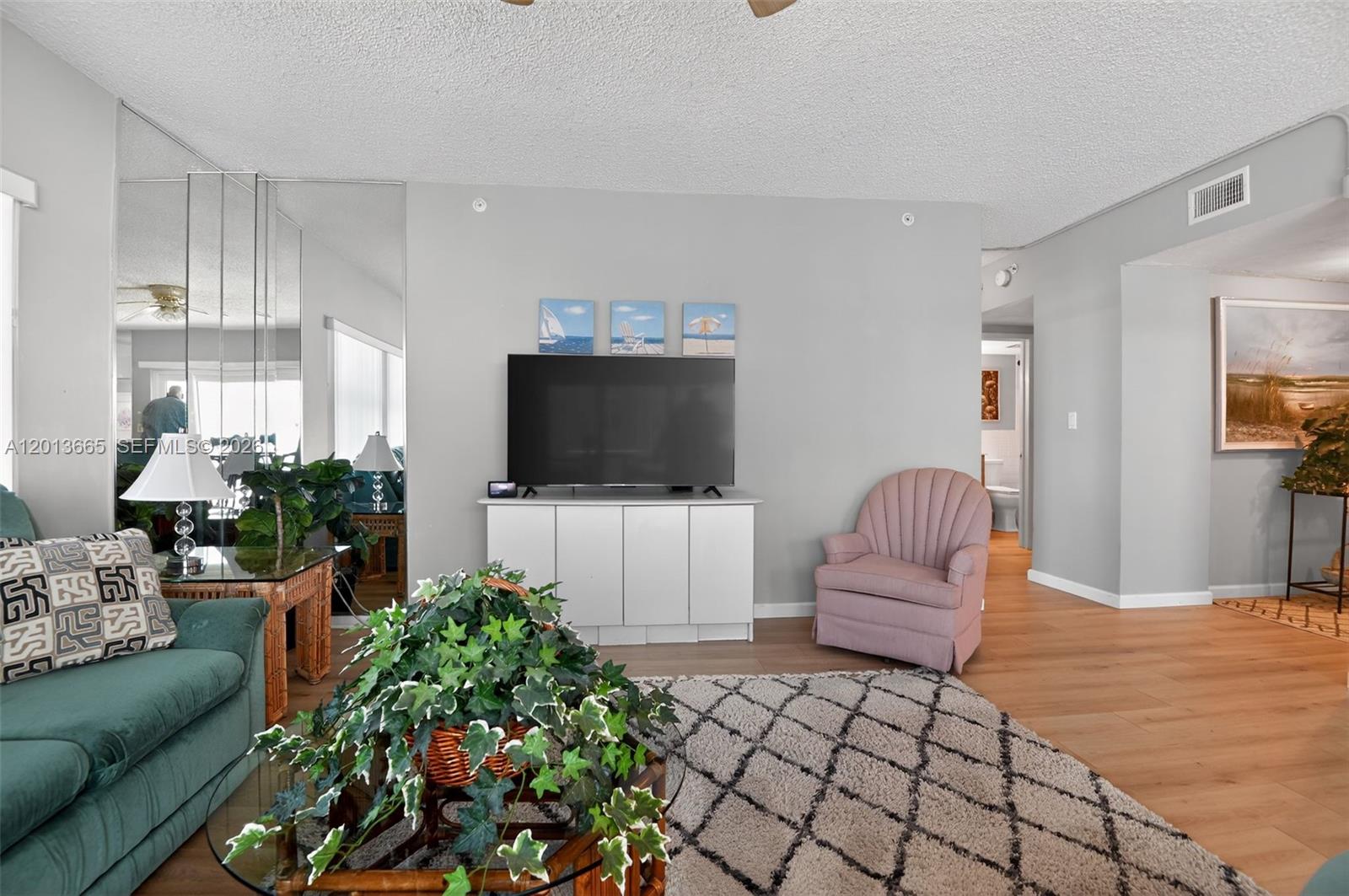 A living room features light gray walls, wood-look flooring, a television console, and a pink chair — 205 Highway A1A Unit 502, Satellite Beach FL 32937, SATELLITE BEACH, FL