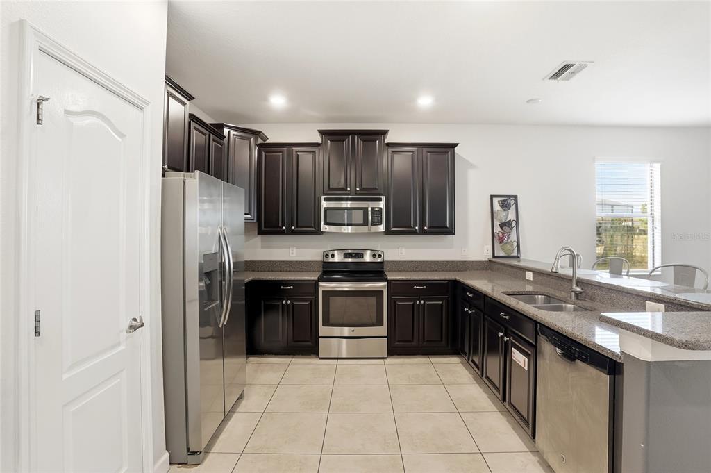 A kitchen features dark wood cabinets, stainless steel appliances, granite countertops, and light tile flooring — 9039 SHADOW MOUNTAIN STREET, DAVENPORT, FL
