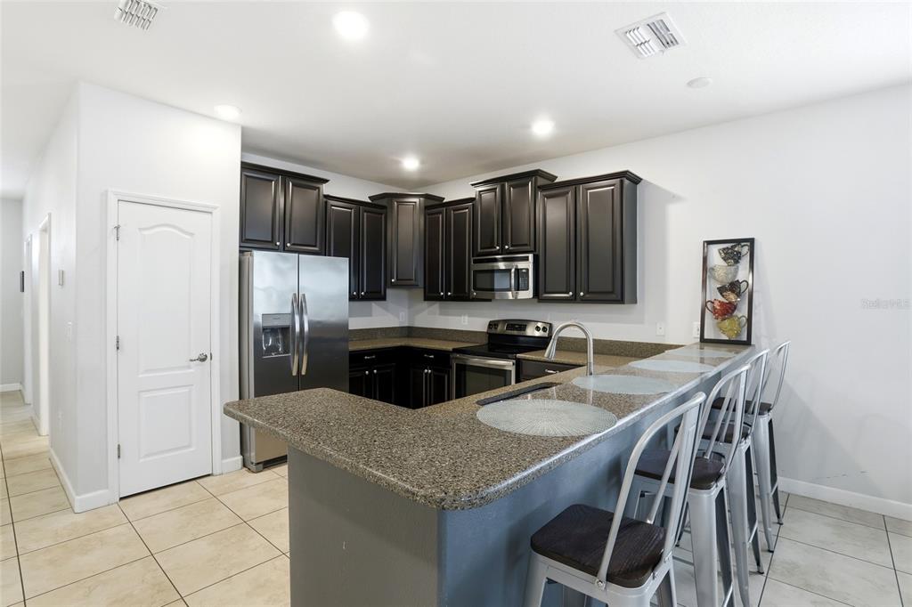 A kitchen features dark wood cabinets, stainless steel appliances, and a granite breakfast bar — 9039 SHADOW MOUNTAIN STREET, DAVENPORT, FL