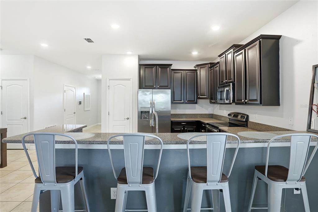 A kitchen features dark wood cabinets, granite countertops, stainless steel appliances, and a breakfast bar — 9039 SHADOW MOUNTAIN STREET, DAVENPORT, FL