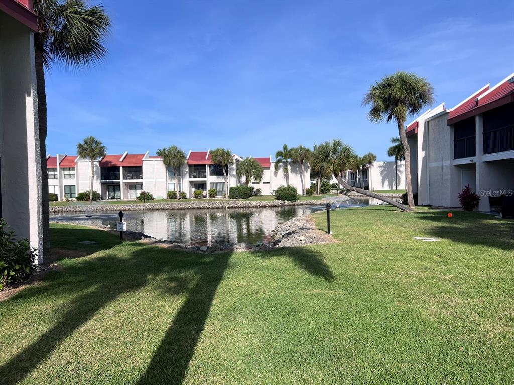A view of a pond surrounded by apartment buildings and palm trees on a sunny day — 1801 GULF DRIVE N UNIT 184, BRADENTON BEACH, FL
