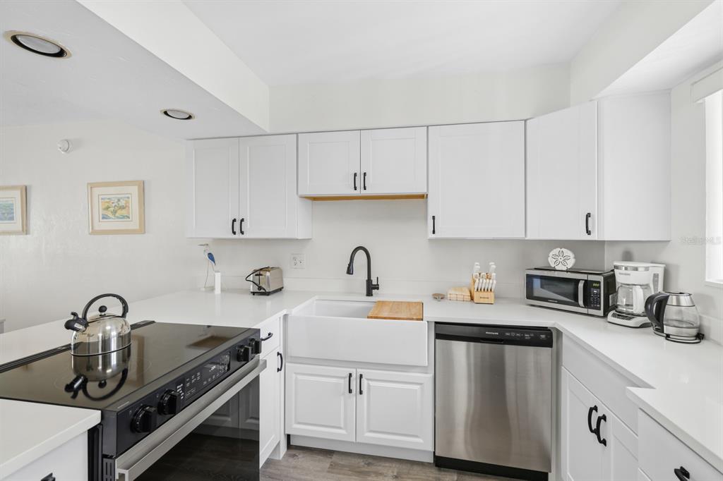 A kitchen with white cabinets and a black stove overlooks an open-concept dining and living area — 1801 GULF DRIVE N UNIT 184, BRADENTON BEACH, FL