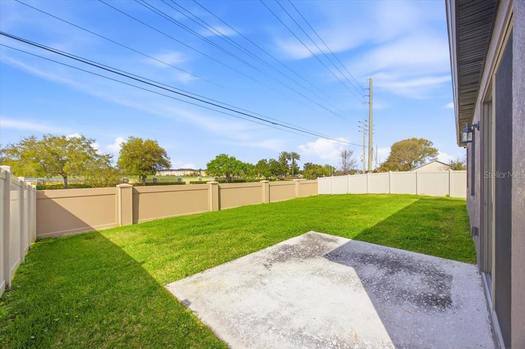A backyard features a concrete patio, green lawn, and tan privacy fencing under a blue sky — 1917 CAYMAN COVE CIRCLE, ST CLOUD, FL