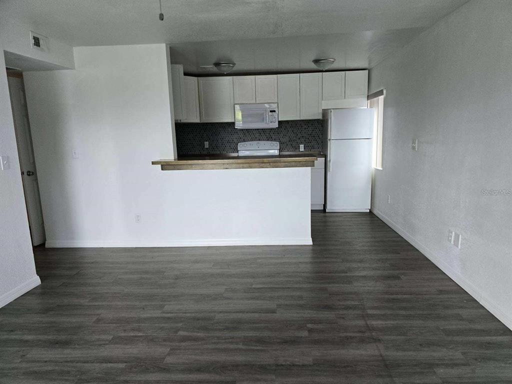 A kitchen with white cabinets and a breakfast bar overlooks a living area with flooring — 800 N FISKE BOULEVARD UNIT 714, COCOA, FL
