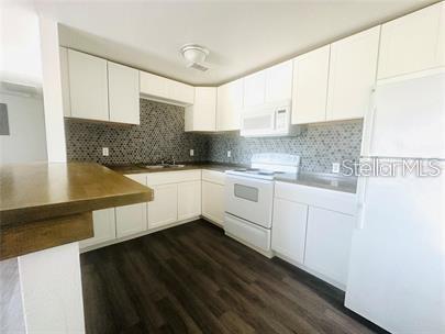 A kitchen features white cabinets, dark wood-look flooring, and a patterned tile backsplash — 800 N FISKE BOULEVARD UNIT 714, COCOA, FL