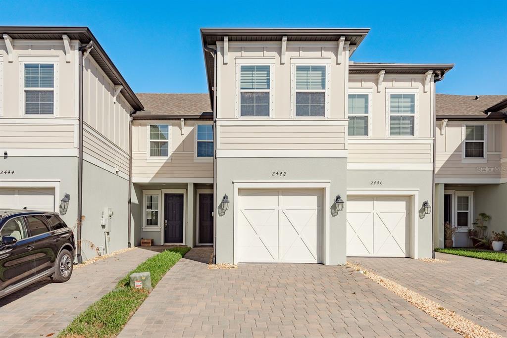 A row of three attached townhomes features light-colored siding, white garage doors, and paved driveways — 2442 FOGGY CREEK CIRCLE, CLEARWATER, FL