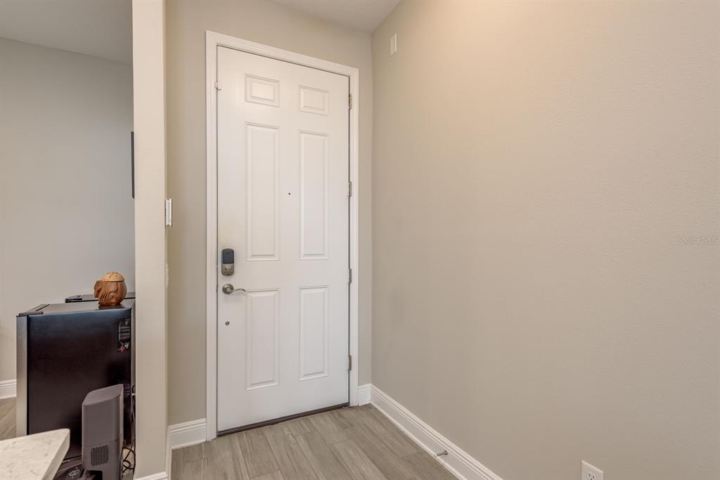 A white front door with a smart lock is set against a plain beige wall — 2442 FOGGY CREEK CIRCLE, CLEARWATER, FL