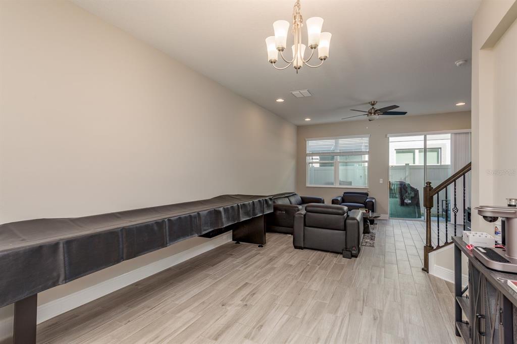 A living room features wood-look tile flooring, a shuffleboard table, and dark leather furniture — 2442 FOGGY CREEK CIRCLE, CLEARWATER, FL
