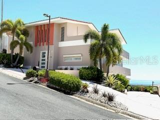 A two-story house with palm trees and a sloped driveway under a clear blue sky — 1 SHELL CASTLE CLUB UNIT 86, HUMACAO, PR