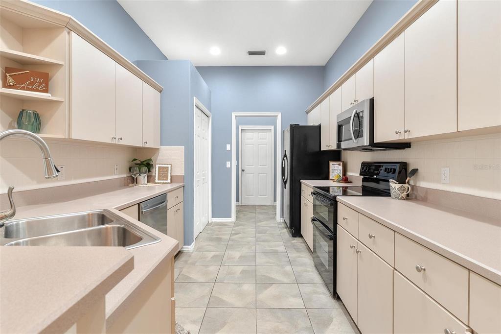 A galley-style kitchen features beige cabinets, light countertops, stainless steel appliances, and tile flooring — 6200 TOPSAIL ROAD, LADY LAKE, FL