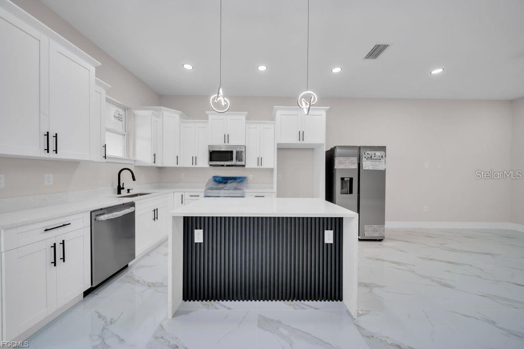 A modern kitchen features white cabinets, a black-paneled island, and white marble-style flooring — 225/227 HOMER AVENUE S, LEHIGH ACRES, FL