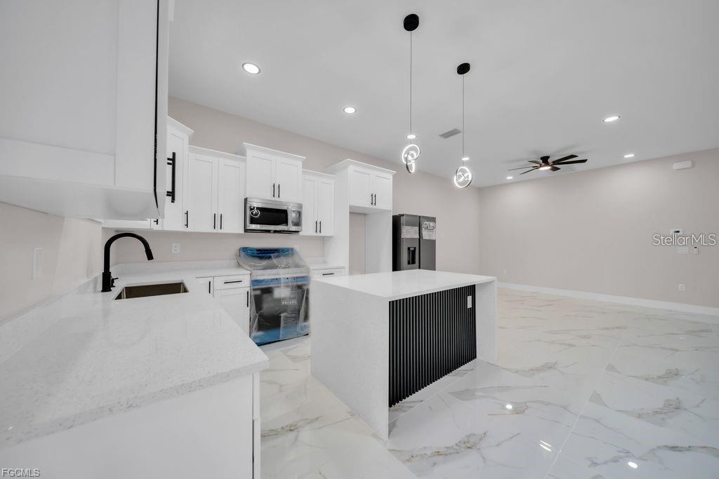 A modern kitchen features white cabinets, a quartz island, and marble-look tile flooring — 225/227 HOMER AVENUE S, LEHIGH ACRES, FL