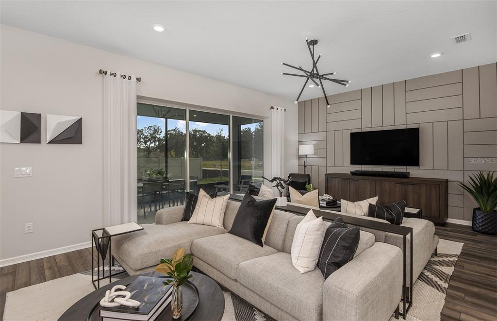 A living room features a sectional sofa, a geometric accent wall, and a sliding glass door — 16820 HARMONY RIVER LANE, PARRISH, FL