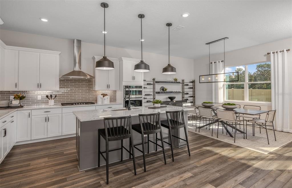 A modern kitchen features white cabinetry, a gray island with bar stools, and an adjacent dining area — 16820 HARMONY RIVER LANE, PARRISH, FL