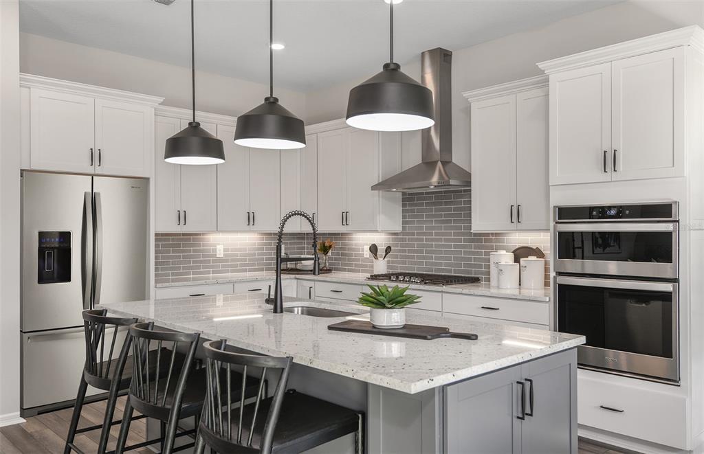 A modern kitchen features white cabinets, a gray island, stainless appliances, and pendant lighting — 16820 HARMONY RIVER LANE, PARRISH, FL