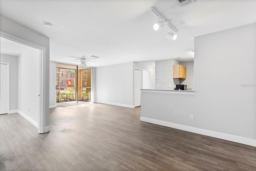 An open-concept living area features light gray walls, wood-look flooring, and a sliding glass door — 7606 PISSARRO DRIVE UNIT 104, ORLANDO, FL