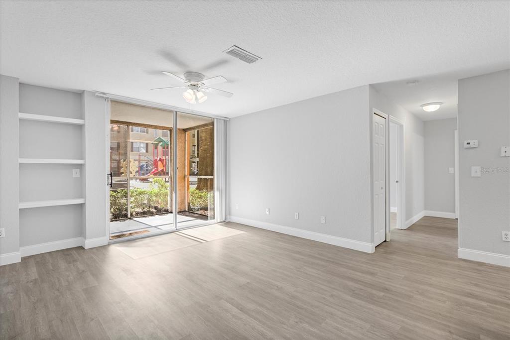 A living room with light wood-look flooring, built-in shelves, and a sliding glass door to a patio — 7606 PISSARRO DRIVE UNIT 104, ORLANDO, FL