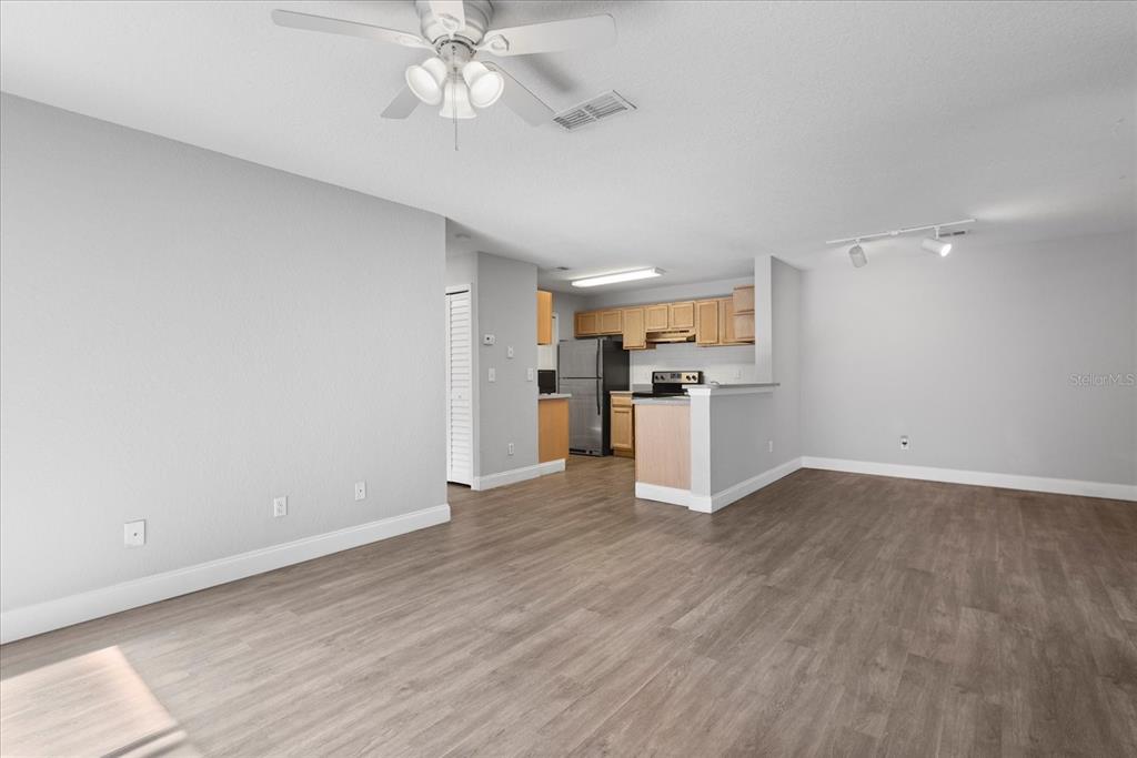 An open-concept living area features light gray walls, wood-look flooring, and an adjacent kitchen — 7606 PISSARRO DRIVE UNIT 104, ORLANDO, FL