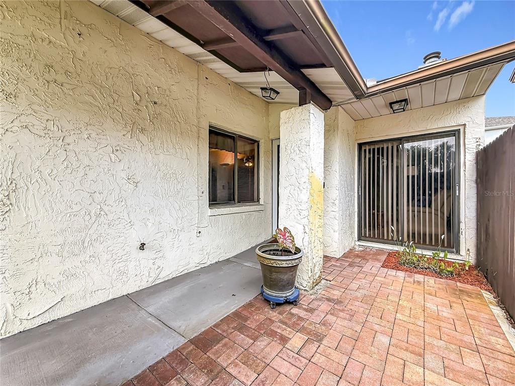 A covered patio features a brick floor, a stucco wall, and a sliding glass door — 2115 KINGS CROSSING SW, WINTER HAVEN, FL