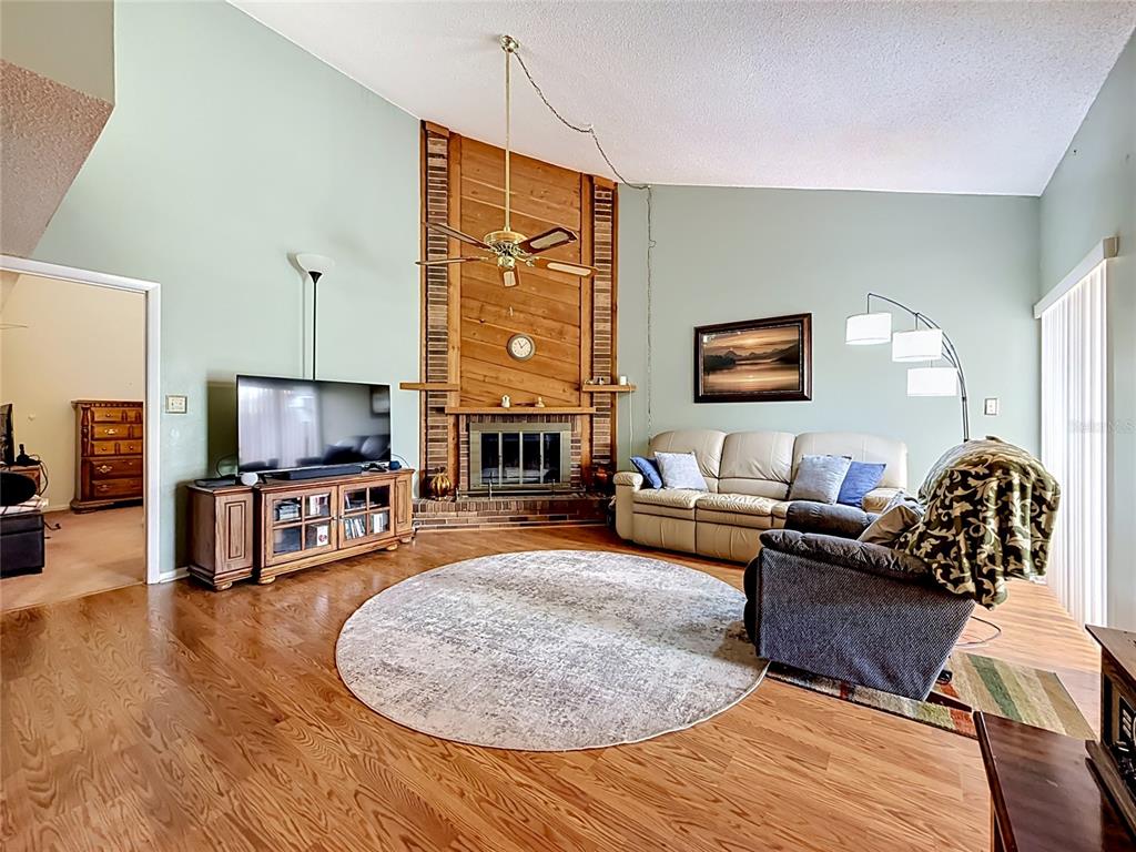 A living room features a wood-paneled fireplace, vaulted ceilings, hardwood floors, and a circular rug — 2115 KINGS CROSSING SW, WINTER HAVEN, FL