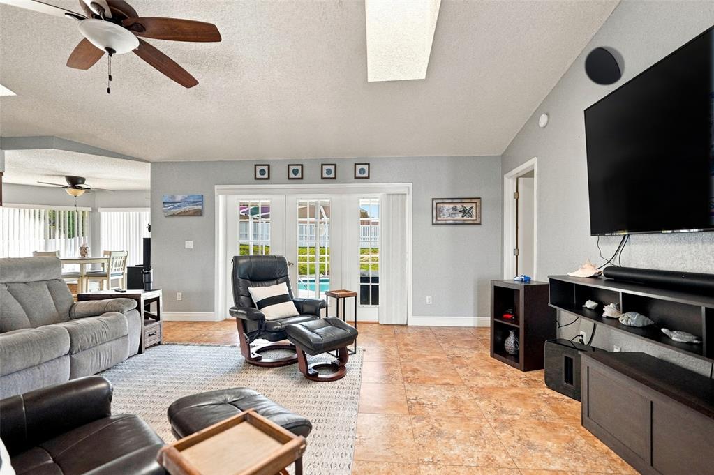 A living room features tile floors, a ceiling fan, a television, and sliding glass doors — 10381 FLAG ROAD, SPRING HILL, FL