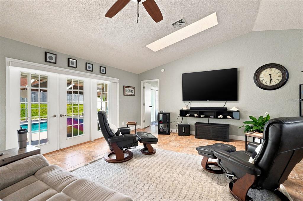 A living room features tiled floors, a large television, two leather recliners, and glass doors — 10381 FLAG ROAD, SPRING HILL, FL