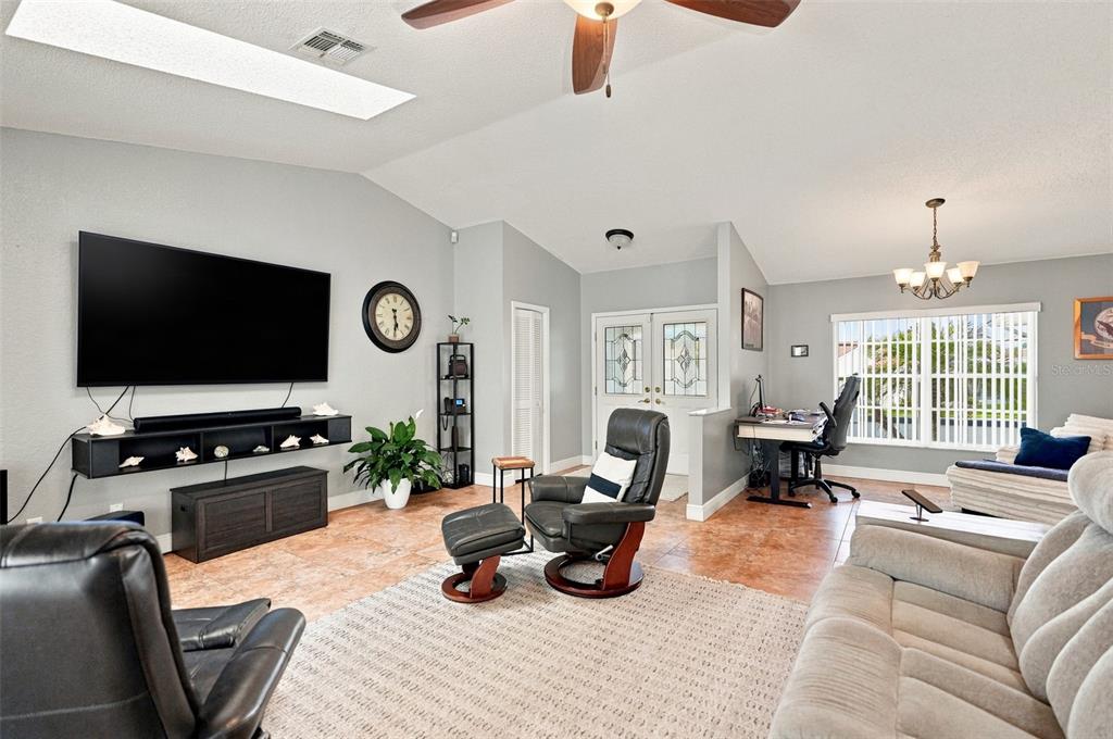 A living room features a large television, leather recliners, tile flooring, and a home office area — 10381 FLAG ROAD, SPRING HILL, FL