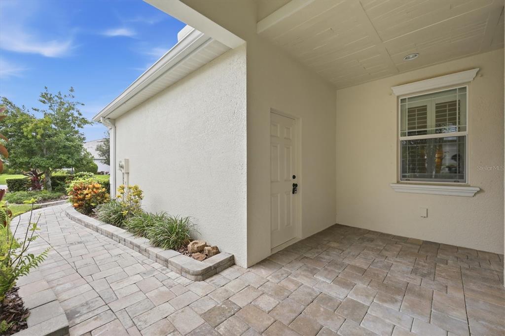 A covered patio with light-colored pavers, a white door, and a window on the wall — 2905 TRUSTEE AVENUE, SARASOTA, FL