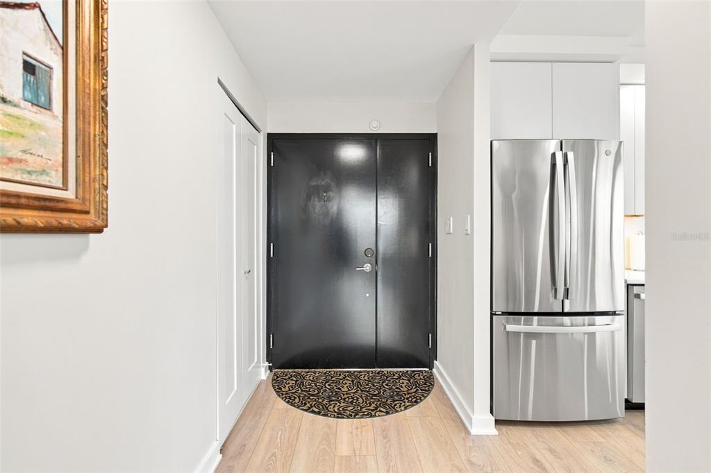 A hallway with light wood flooring, a black double door, and a stainless steel refrigerator — 707 S GULFSTREAM AVENUE UNIT 207, SARASOTA, FL