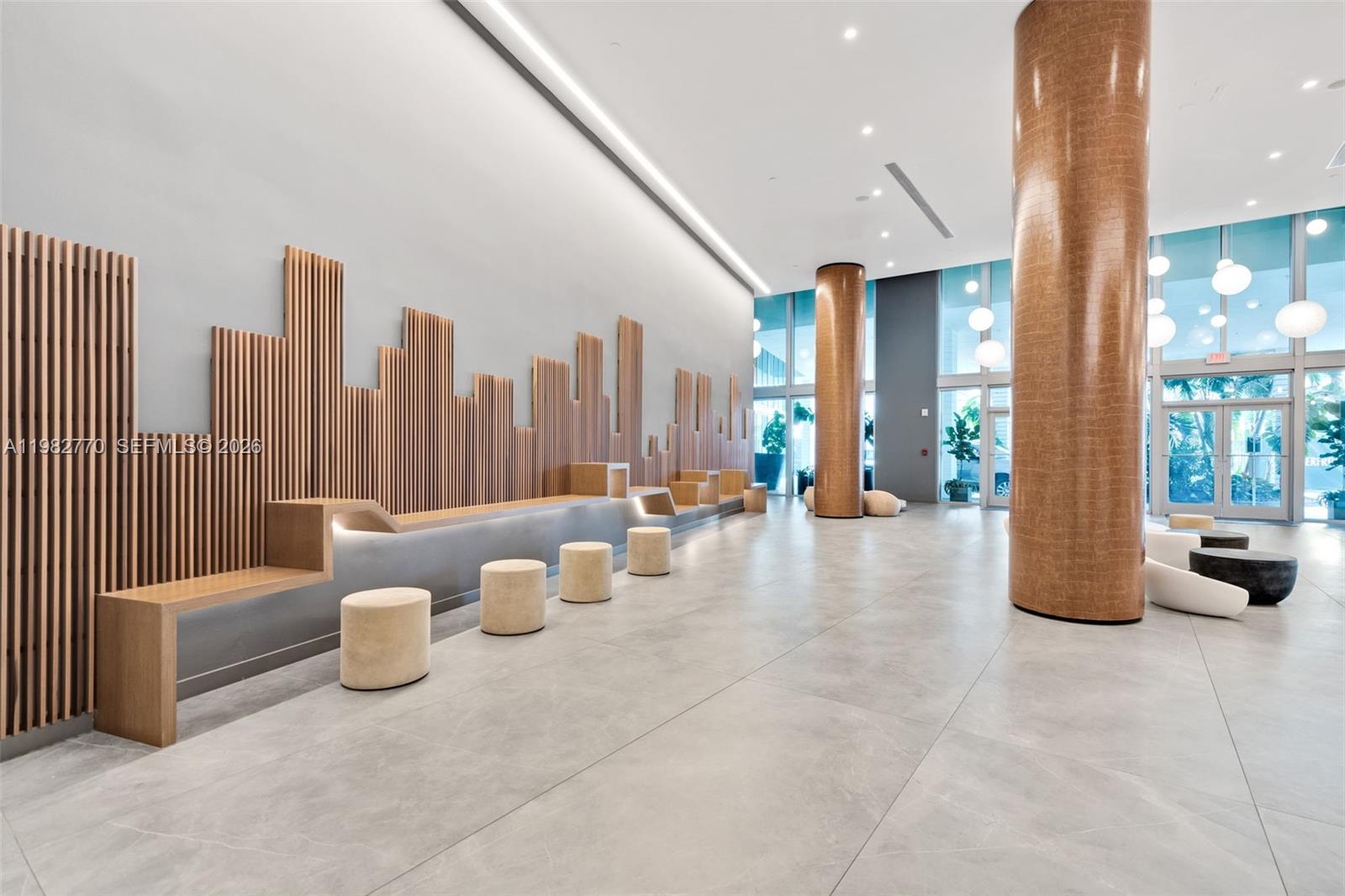 A modern lobby features large cylindrical columns, gray tile flooring, and contemporary white seating — 350 S Miami Ave # 2412, Miami FL 33130, MIAMI, FL