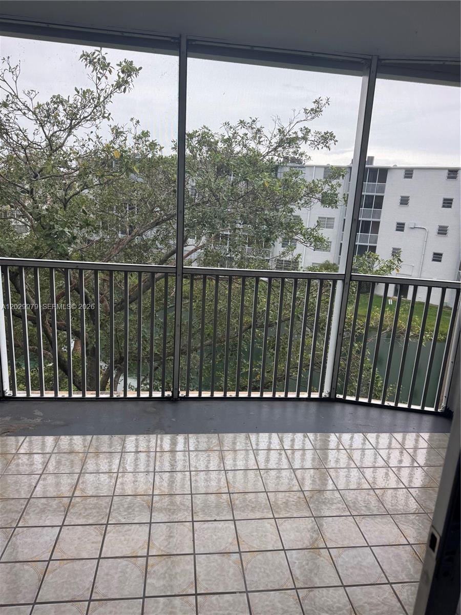 A screened-in balcony features tiled flooring and a view of trees and a nearby building — 1710 NE 191st St # 3, Miami FL 33179, MIAMI, FL