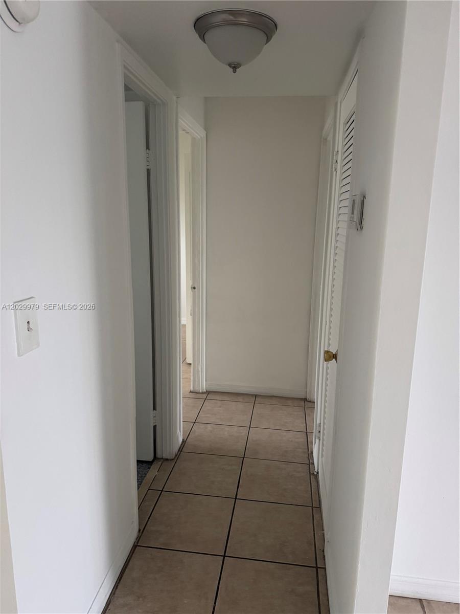 A narrow hallway features beige tile flooring, white walls, and a central ceiling light fixture — 1710 NE 191st St # 3, Miami FL 33179, MIAMI, FL