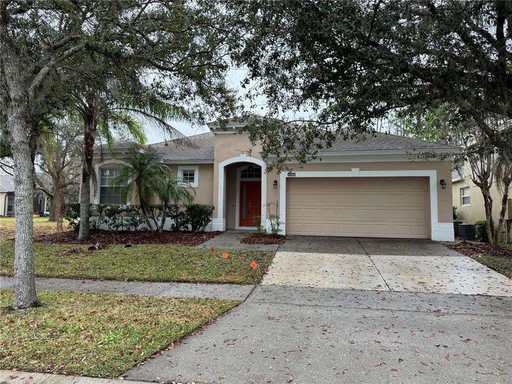 A single-story tan house with a two-car garage and a red front door — 10360 SANDY MARSH LANE, ORLANDO, FL