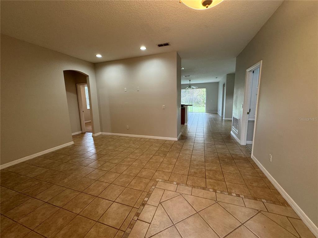 An open-concept living area features tan tile flooring, recessed lighting, and a view toward the kitchen — 10360 SANDY MARSH LANE, ORLANDO, FL