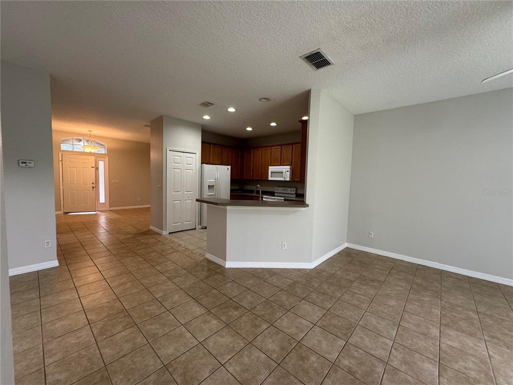 A kitchen with wood cabinets and a breakfast bar overlooks a tiled living area — 10360 SANDY MARSH LANE, ORLANDO, FL