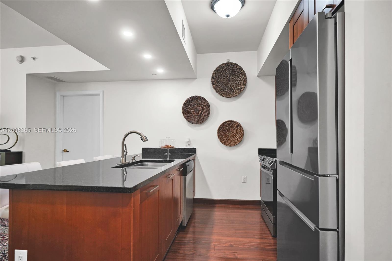A kitchen features dark wood cabinets, black granite countertops, stainless steel appliances, and woven wall decor — 4100 Salzedo St # 411, Coral Gables FL 33146, CORAL GABLES, FL