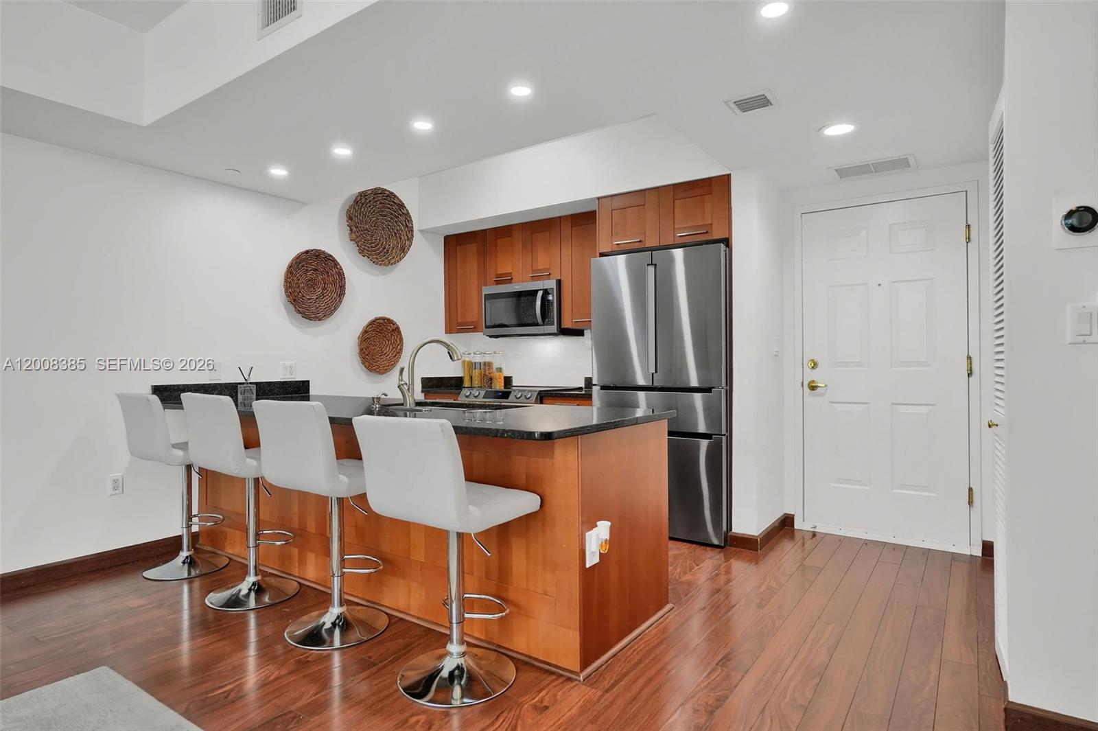 A kitchen features wooden cabinets, stainless steel appliances, a dark countertop, and four bar stools — 4100 Salzedo St # 411, Coral Gables FL 33146, CORAL GABLES, FL
