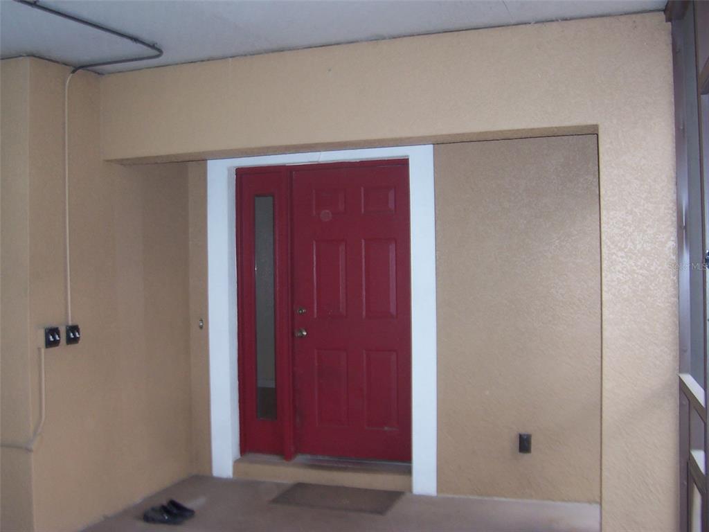 A red front door with a side light is set into a beige stucco wall — 37544 TUCKER ROAD, ZEPHYRHILLS, FL