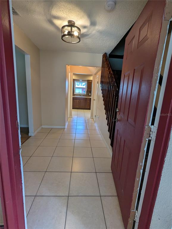 An entryway with tiled floors leads to a kitchen, featuring a staircase with wooden railings — 37544 TUCKER ROAD, ZEPHYRHILLS, FL