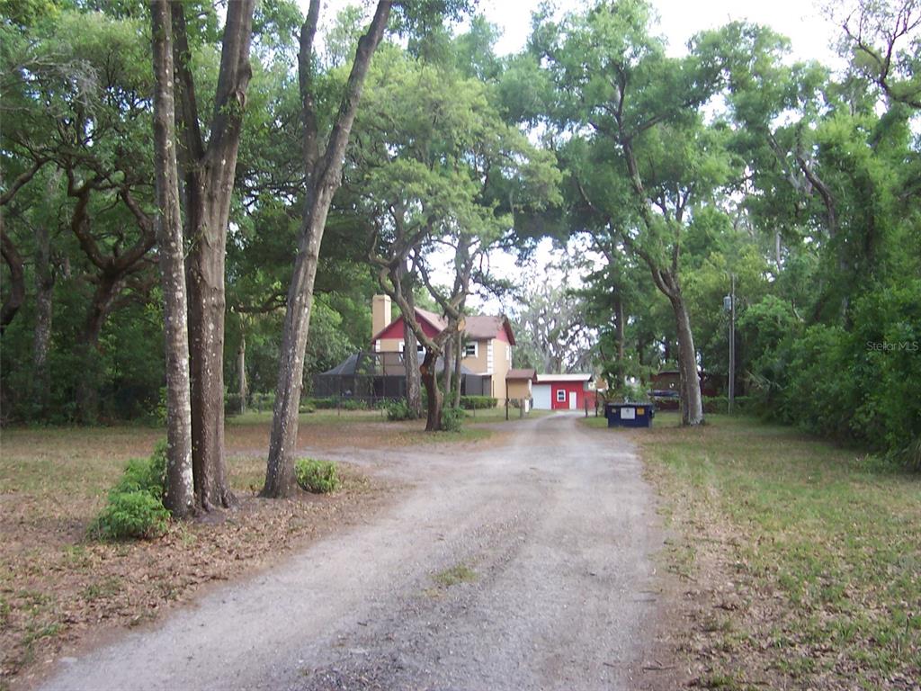 A gravel driveway leads to a two-story house with a red garage and surrounding trees — 37544 TUCKER ROAD, ZEPHYRHILLS, FL
