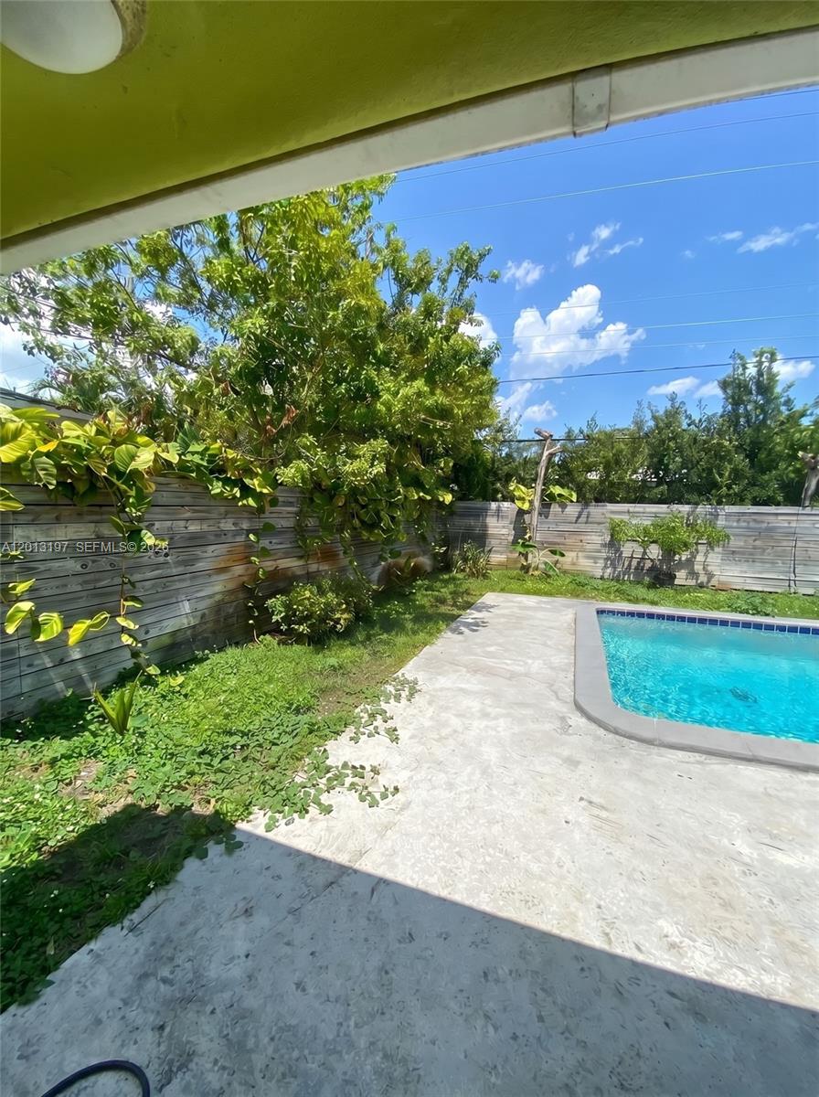 A backyard features a swimming pool, a concrete patio, and a wooden fence with greenery — 21335 NE 19th Ct, Miami FL 33179, MIAMI, FL