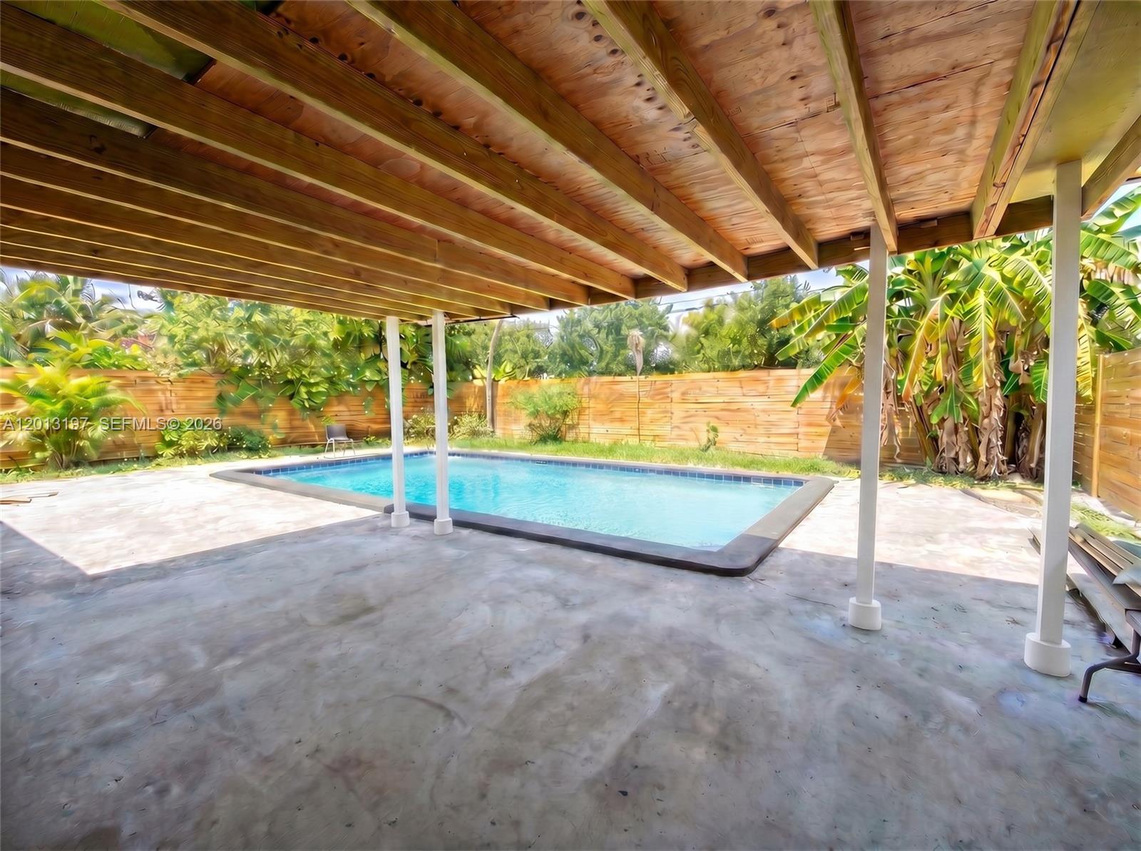 A covered concrete patio overlooks a rectangular swimming pool in a fenced backyard — 21335 NE 19th Ct, Miami FL 33179, MIAMI, FL